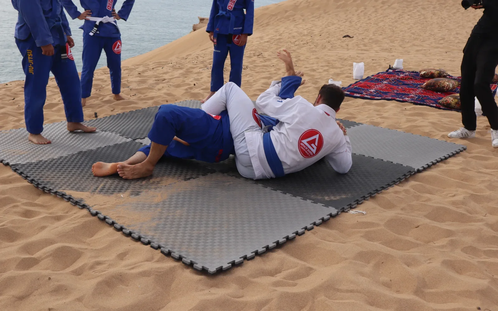 Two participants drilling in gis on mats laid on the sand — previous MatnWave edition