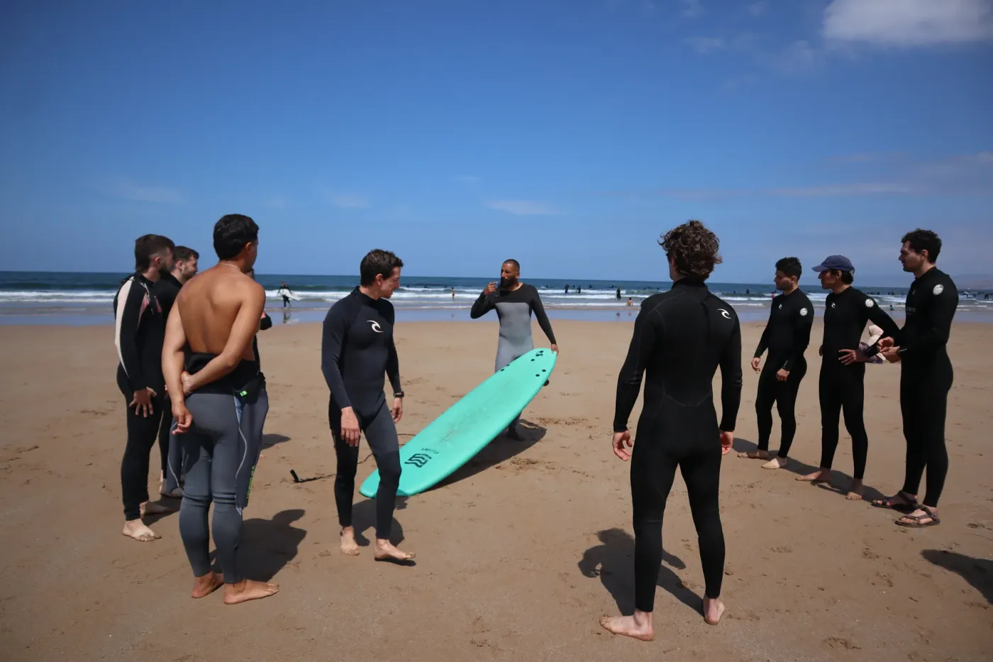 Surf group gathered around a turquoise board for a beach briefing