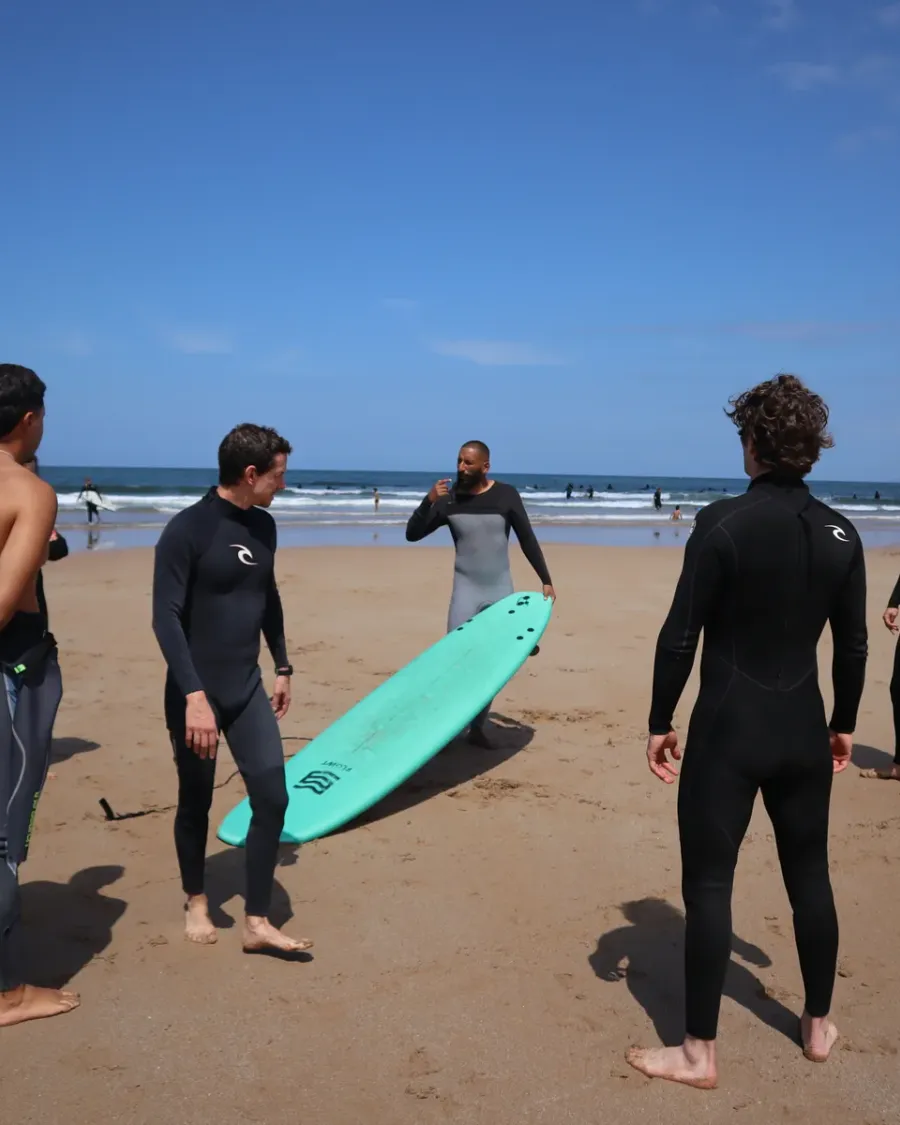 Surf group gathered around a turquoise board for a beach briefing
